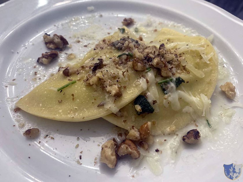 Ravioli ripieni di ricotta e pesto con caciocavallo e noci su letto di parmigiano