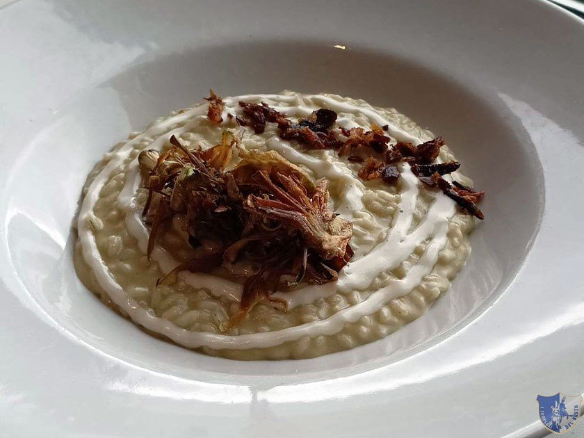 Il risotto mantecato con salsa ai carciofi riduzione di caciocavallo pancetta croccante e chips di carciofi